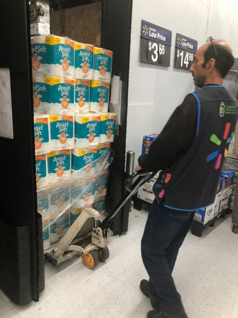 A Walmart associate wheels out a pallet of toilet paper out onto the sales floor.