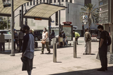 Masked pedestrians wait at a bus stop in Koreatown.