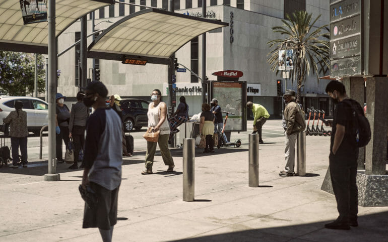 Masked pedestrians wait at a bus stop in Koreatown.