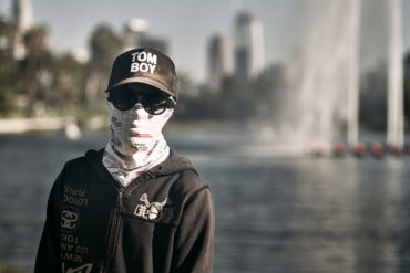 A person stops for a photo while wearing a face covering, sunglasses and a hat.