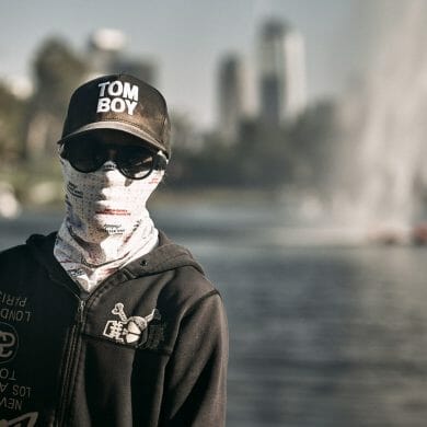 A person stops for a photo while wearing a face covering, sunglasses and a hat.