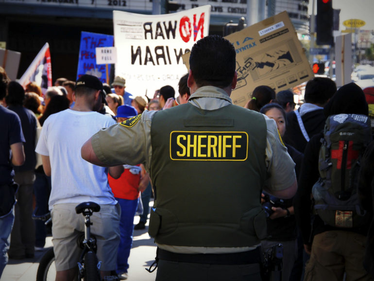A Los Angeles Sheriffâ€™s Department deputy watches a crowd at an anti-war protest in 2012.