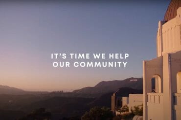 A shot of Griffith Observatory with the Hollywood sign in the distant background. In the center is overlayed white text that says, "It's time we help our community."