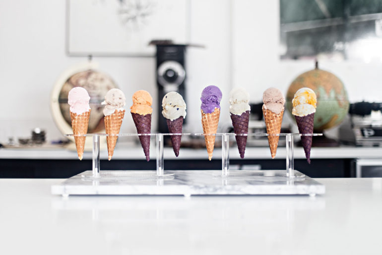 A row of eight colorful ice cream cones on a countertop cone holder.