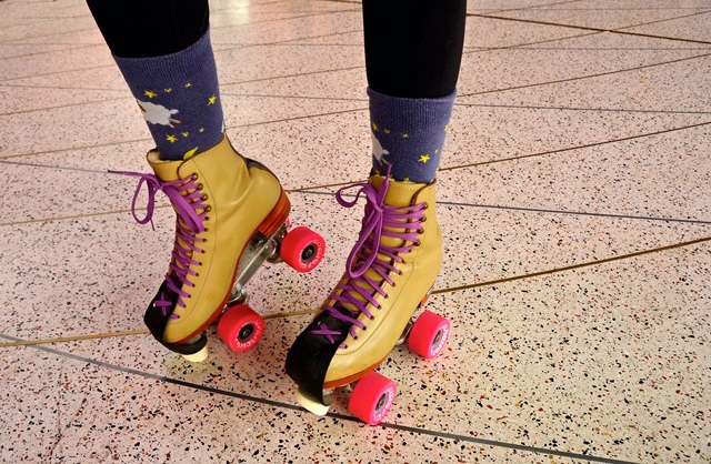 A close-up shot of a person wearing bright yellow roller skates with neon-orange wheels and purple laces.