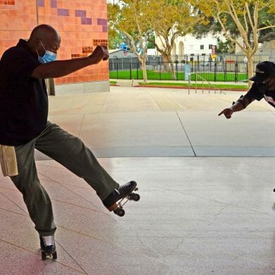 Two adult men balance mid-motion on their roller skates at an outdoor park.