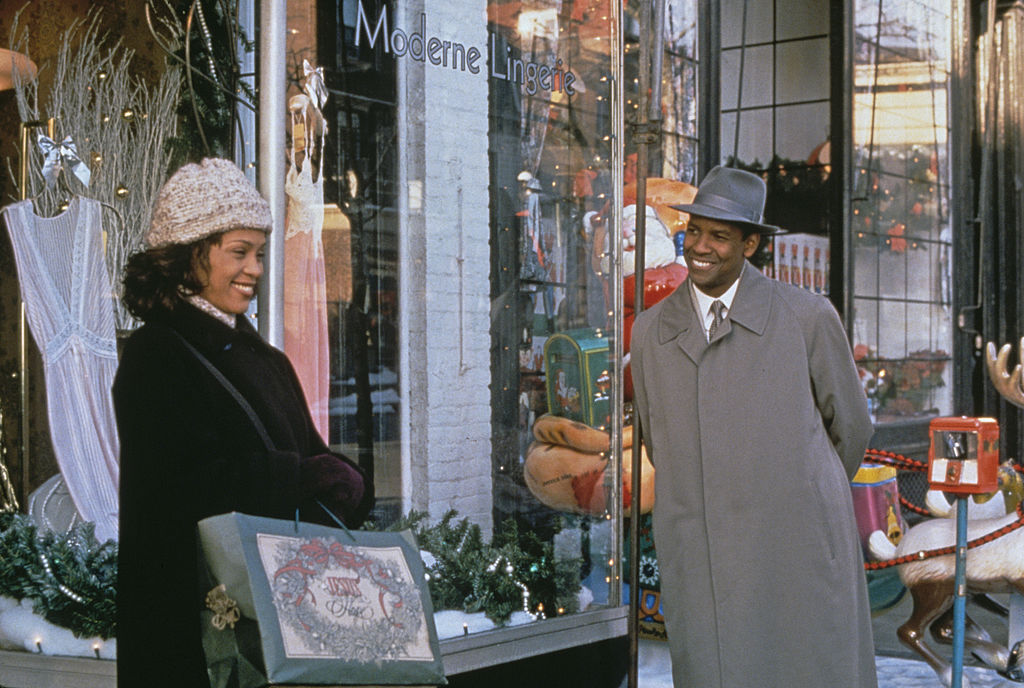 A woman leans against a store window with a shopping bag as a man talks to her, both smiling.