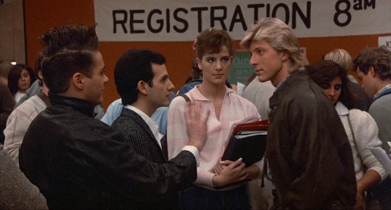 Two teenage boys confront each other in a crowded high school building.