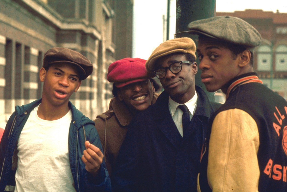 Four high school boys in 1960s outfits and hats smile and smirk at the camera.
