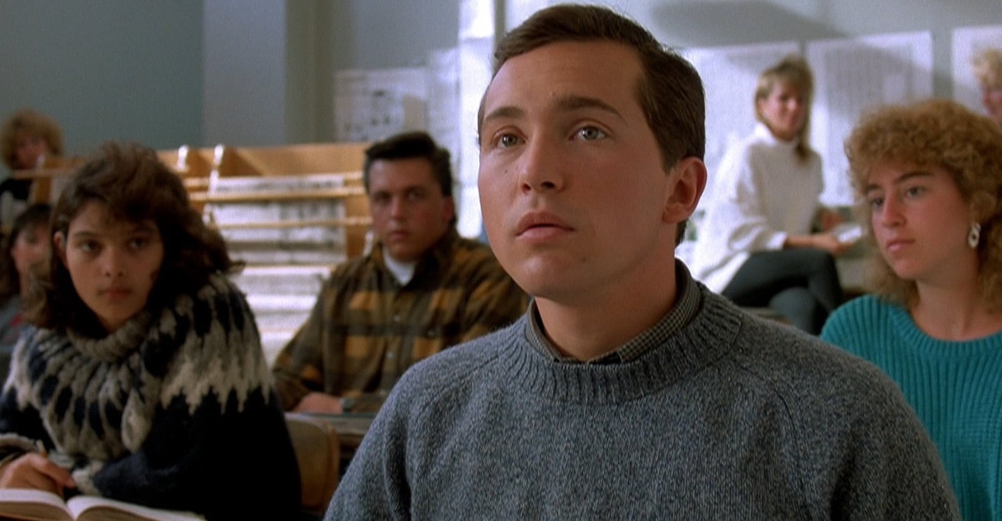 A pensive student sits in a desk and stares at something off-camera.