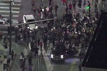 A nighttime overhead photo of an intersection crowded with people on foot. A white Prius is beginning to drive through the crowd.