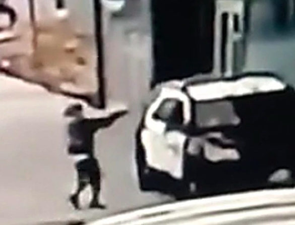 Low-quality surveillance footage that shows a figure pointing a gun into a parked car.