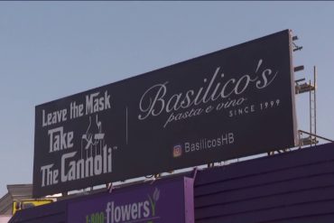 A billboard reading: "Leave the Mask Take the Cannoli," a puppet master illustration from the film "The Godfather" and Basilico's Pasta e Vino's restaurant information.