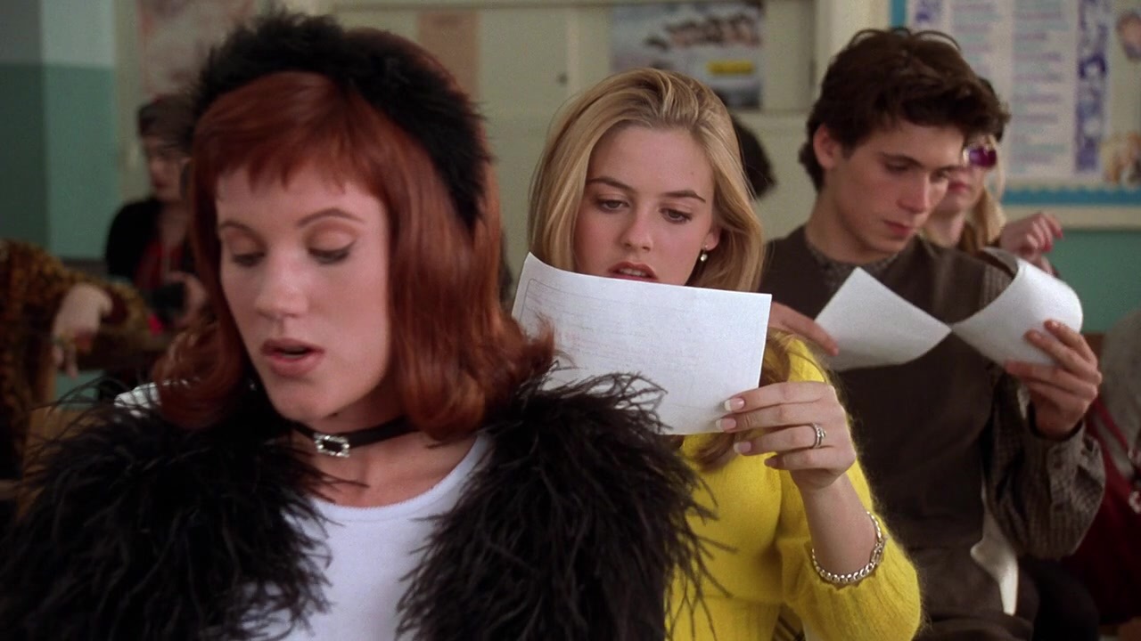 From the movie "Clueless," three high schoolers sit in a row of desks and hold up papers to their faces.