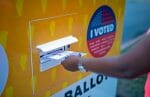 A person deposits their ballot at an official drop box.